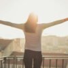 A woman stands with outstretched arms on a sunny balcony, embracing the morning light.