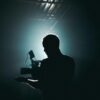Silhouette of a cinematographer with camera gear in a dramatic, low light setting.