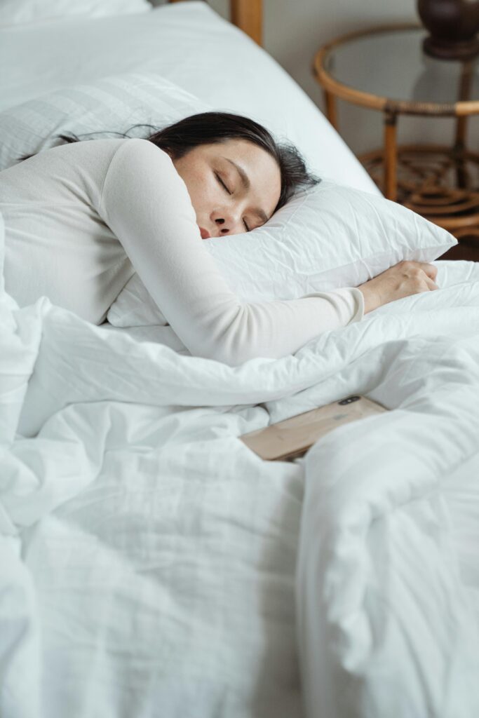 Woman in a cozy bedroom sleeping peacefully, surrounded by white bedding for ultimate comfort, scripturereel.com