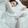 Woman in a cozy bedroom sleeping peacefully, surrounded by white bedding for ultimate comfort, scripturereel.com