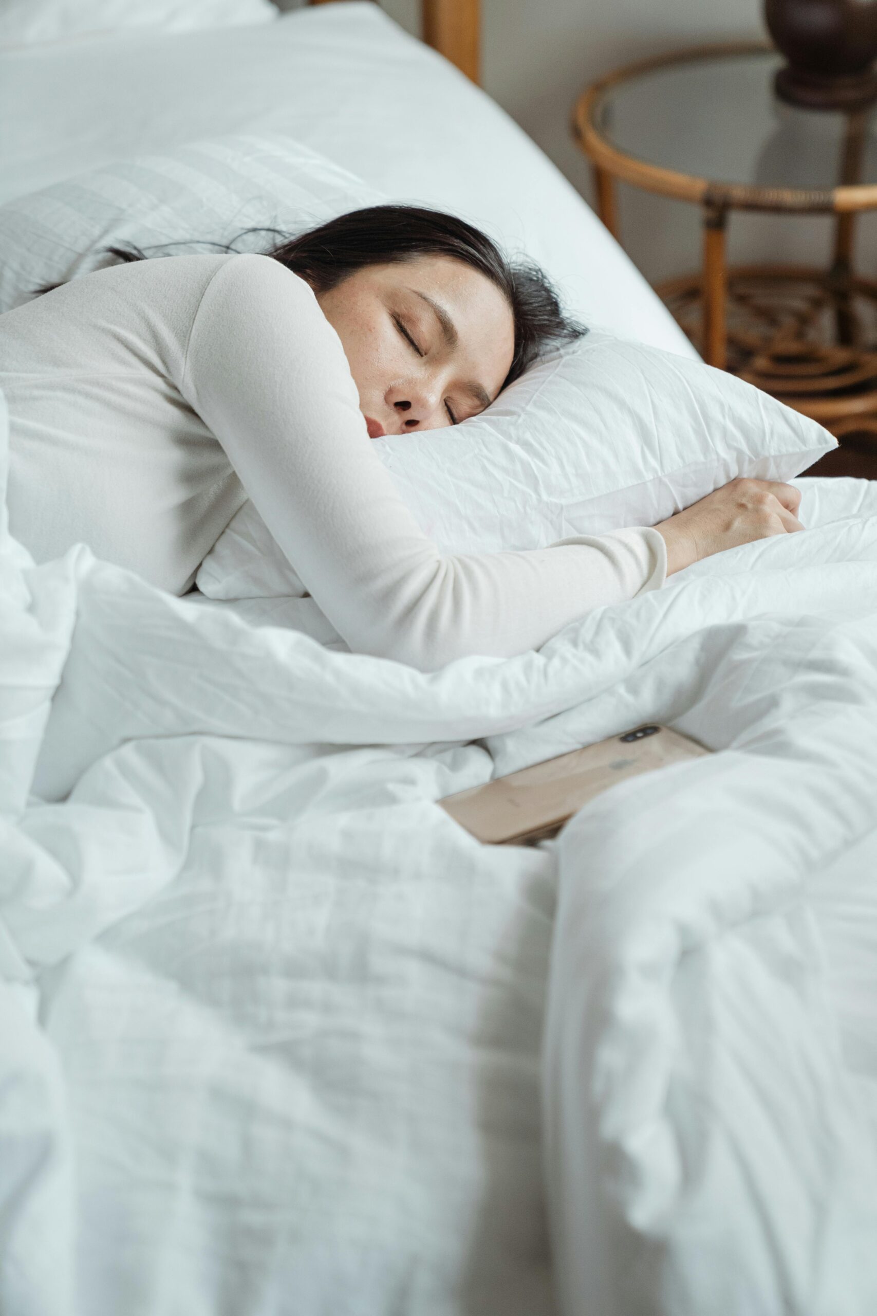 Woman in a cozy bedroom sleeping peacefully, surrounded by white bedding for ultimate comfort, scripturereel.com