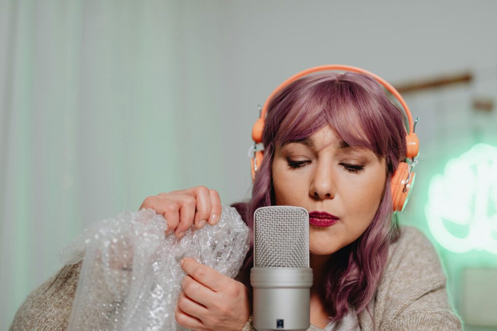 A woman with purple hair performs ASMR using bubble wrap and a microphone.,scripturereel.com