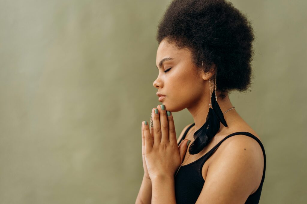 A young woman with afro hair practicing calming meditation indoors. scripturereel.com