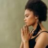 A young woman with afro hair practicing calming meditation indoors. scripturereel.com