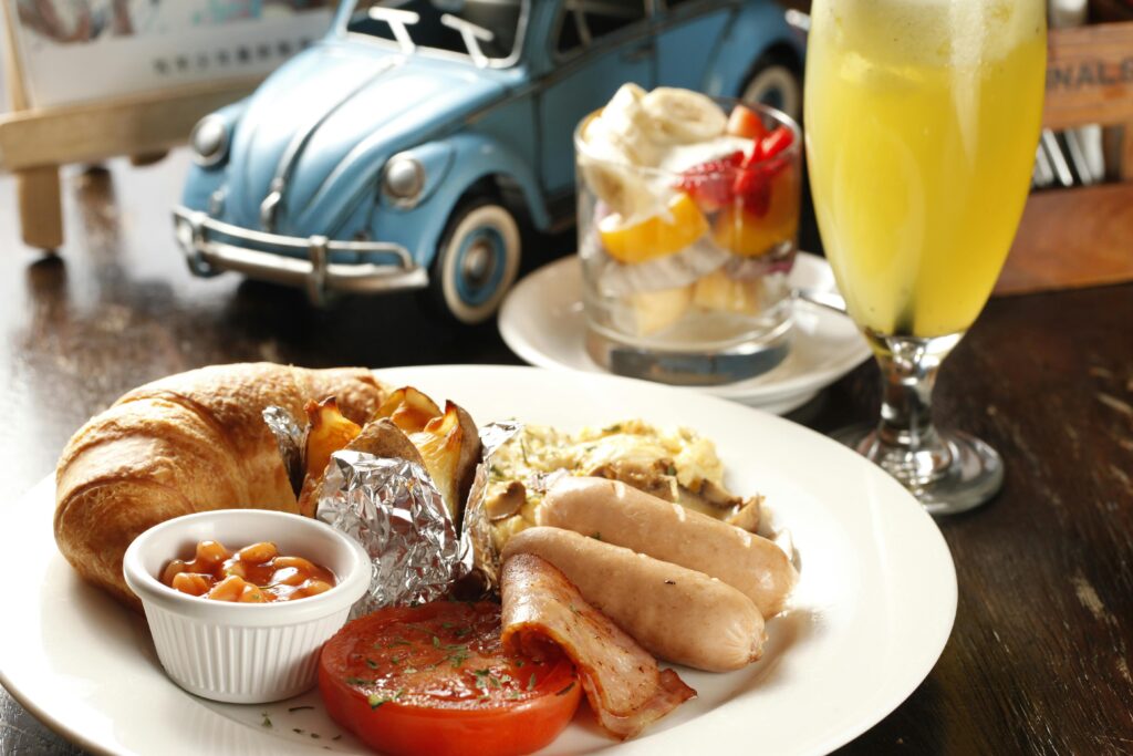 Tasty English breakfast featuring sausages, beans, croissant, and juice on a wooden table.