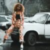 Stylish woman in floral suit posing against a classic car on a rainy day.